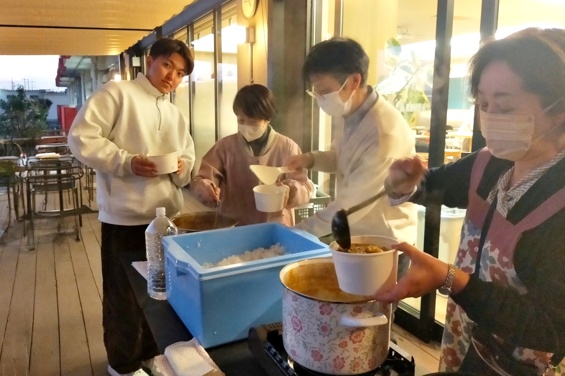 教員が屋外テラスで学生にカレーを提供している様子